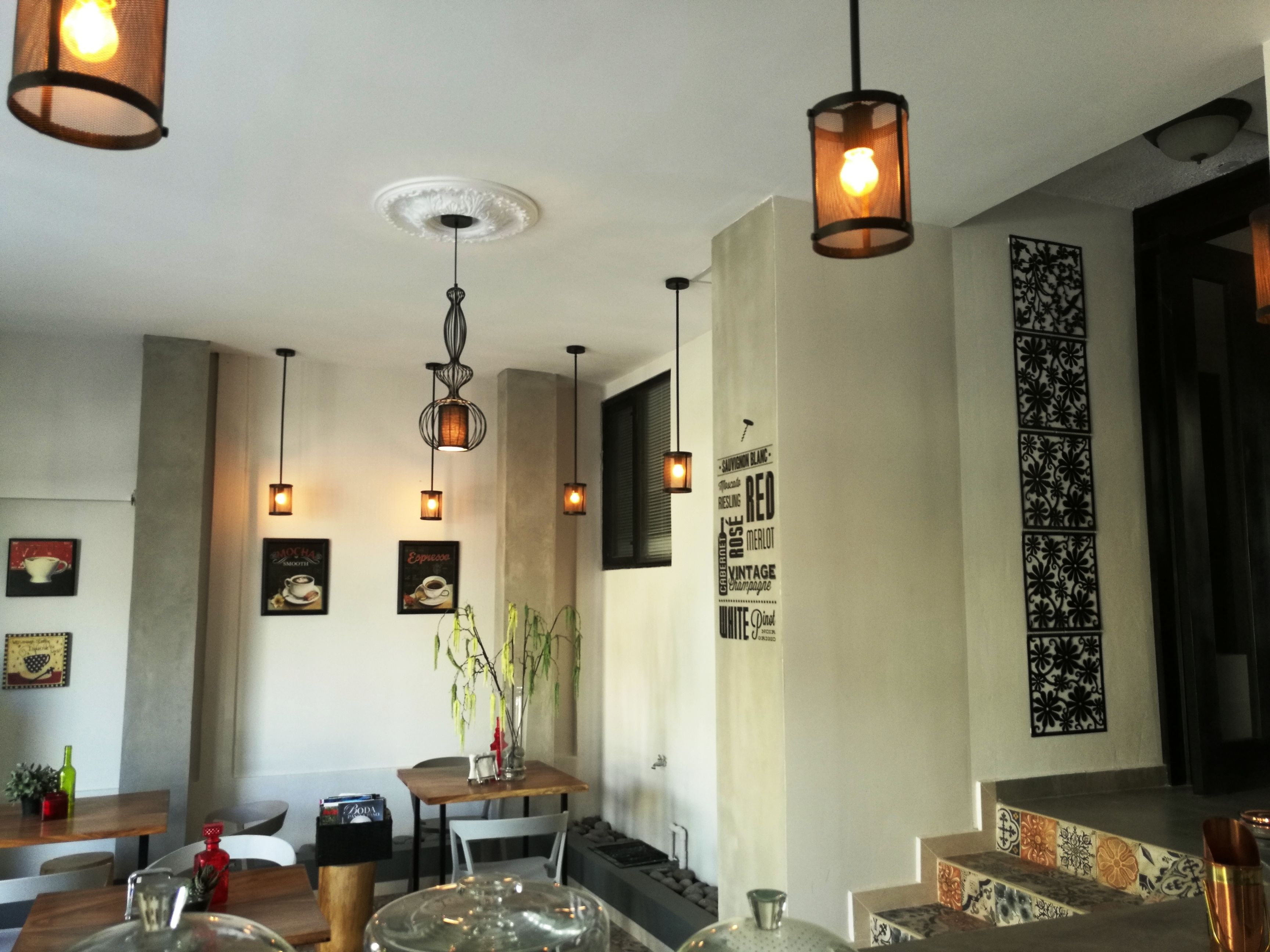 Un comedor moderno con lámparas colgantes, una mesa central con sillas y una pared decorativa con texto y diseños.