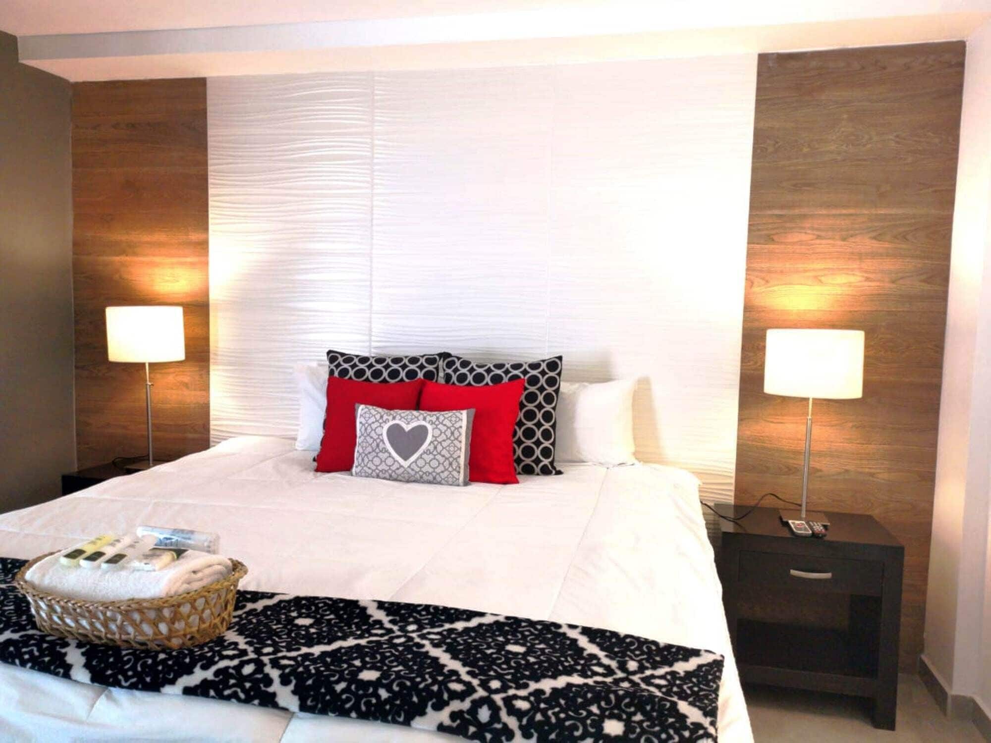 A neatly made bed with a patterned throw, two bedside lamps, and a bedside table with a phone and remote control.