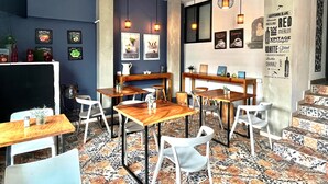 A modern cafe with wooden tables and chairs, a tiled floor, and wall-mounted light fixtures. - Hotel Boutique Valverde Santa Elena (Antiguo Cuscatlán)