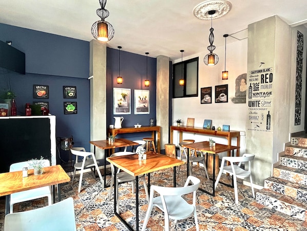 A modern cafe with wooden tables and chairs, a tiled floor, and wall-mounted light fixtures.