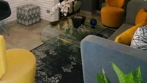 A modern living room with a glass coffee table, a sofa, and two chairs. There is a door with glass panels and a plant on the windowsill. - Hotel Boutique Valverde Santa Elena (Antiguo Cuscatlán)