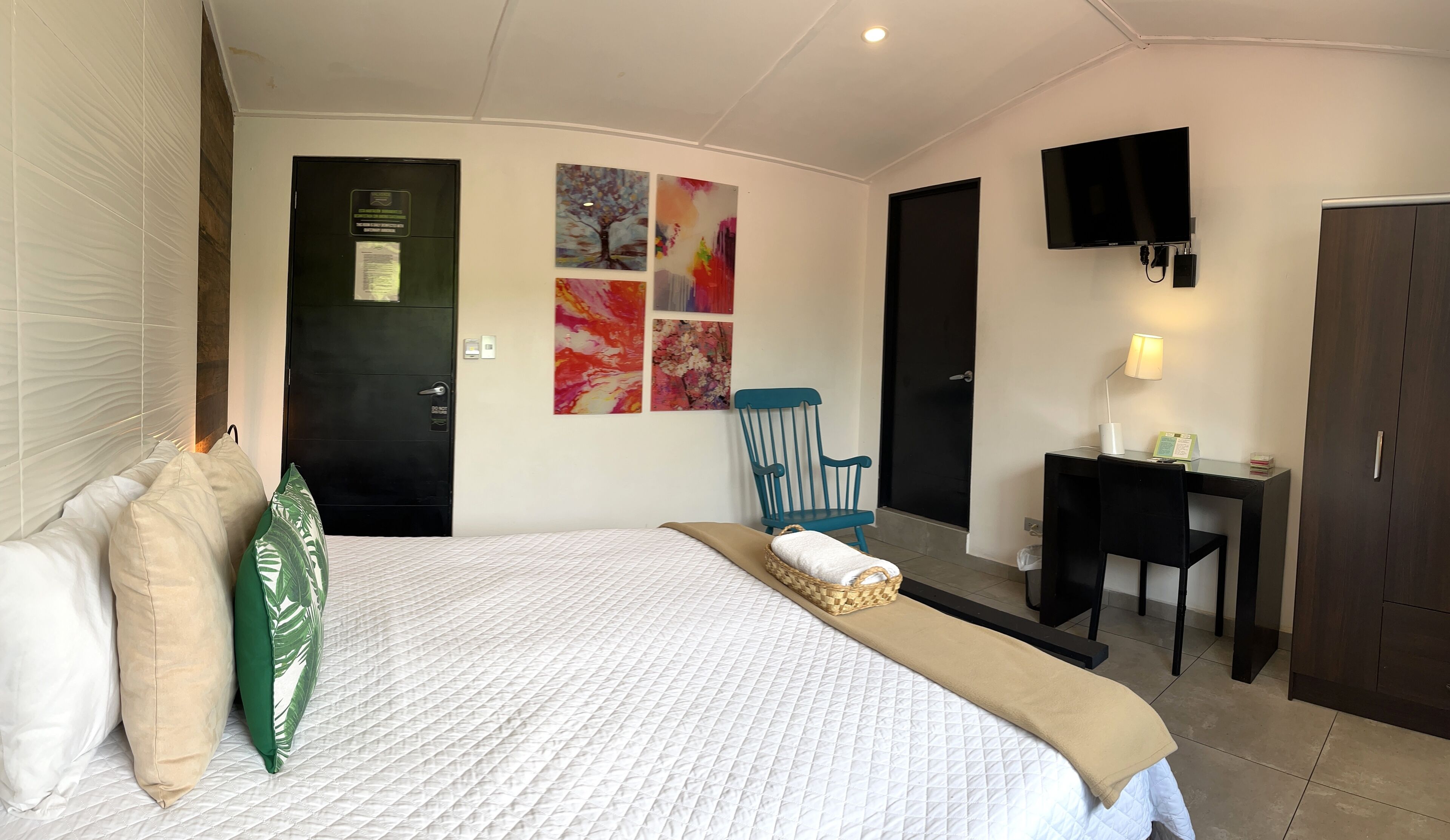 Une chambre d’hôtel avec un lit, un bureau, une chaise, une télévision et des œuvres d’art accrochées au mur.
