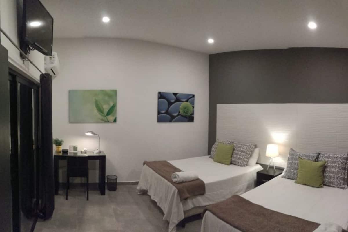 Ein Hotelzimmer mit zwei Betten, einem Schreibtisch, einem Sessel, einer Lampe und Bildern an den Wänden.