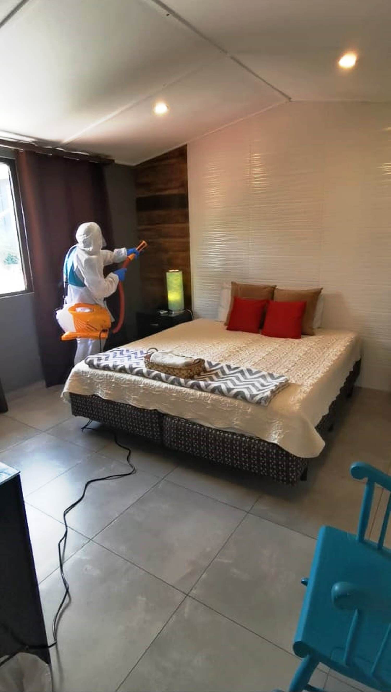 A bedroom with a bed, a bedside table, a lamp, and a person cleaning.