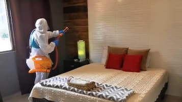 A bedroom with a bed, a bedside table, a lamp, and a person cleaning.