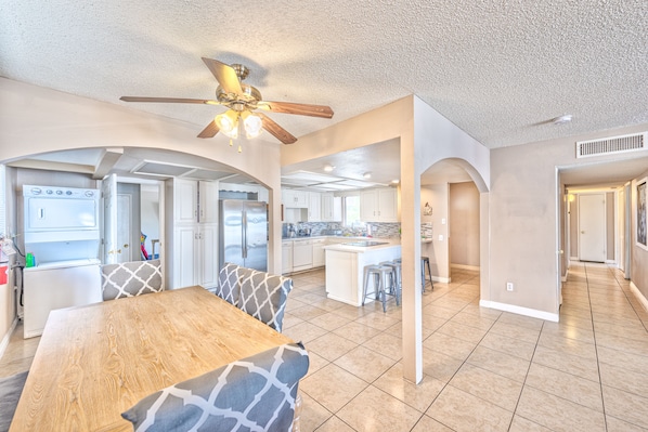 A spacious kitchen with modern appliances, an island, and a dining area with a wooden table and patterned cushions.