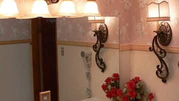 A bathroom with a double sink, a mirror with wall sconces, and a potted plant with red flowers.
