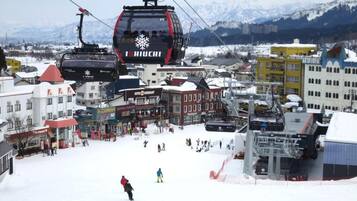 A ski lift with the name "Schiuchi" in a snowy town with buildings and mountains in the background.
