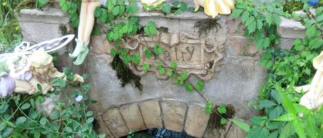 Un jardín con un puente de piedra, estatuas de hadas y exuberante vegetación.