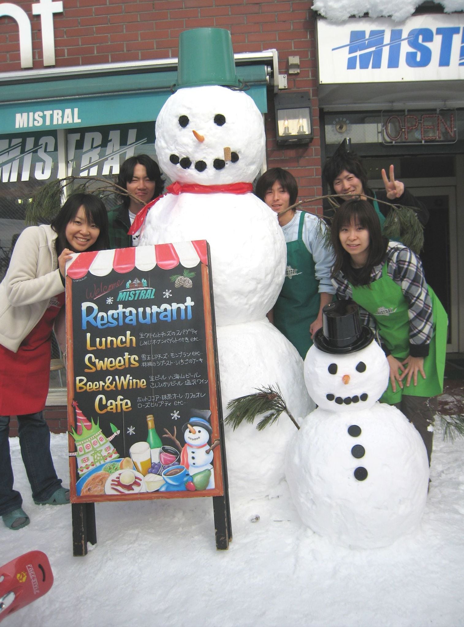 A snowman with a sign in front of a restaurant named Mistral.