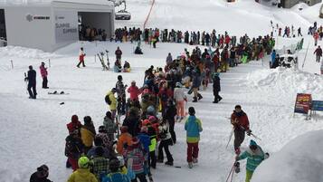 A ski resort with a large crowd gathered near a ski lift, surrounded by snow-covered trees and buildings.