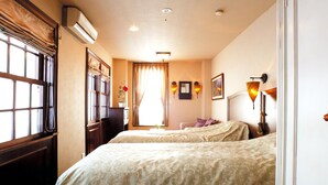 Habitación de hotel con dos camas, una ventana con cortinas, una mesita de noche con lámpara y un espejo adosado a la pared.