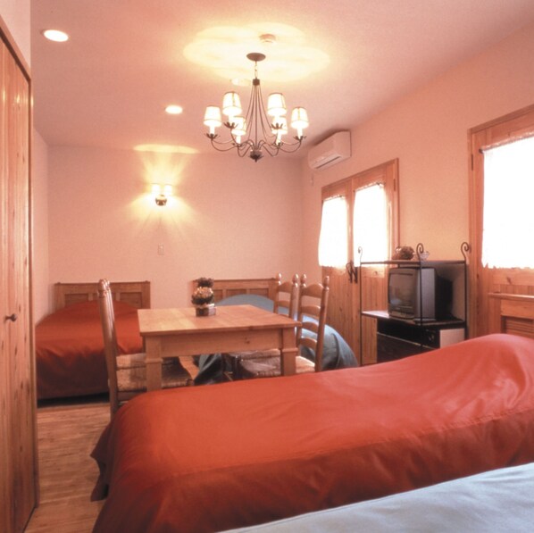 A cozy room with a bed, a wooden table, chairs, a television, and a chandelier. - Mistral (Minamiuonuma)