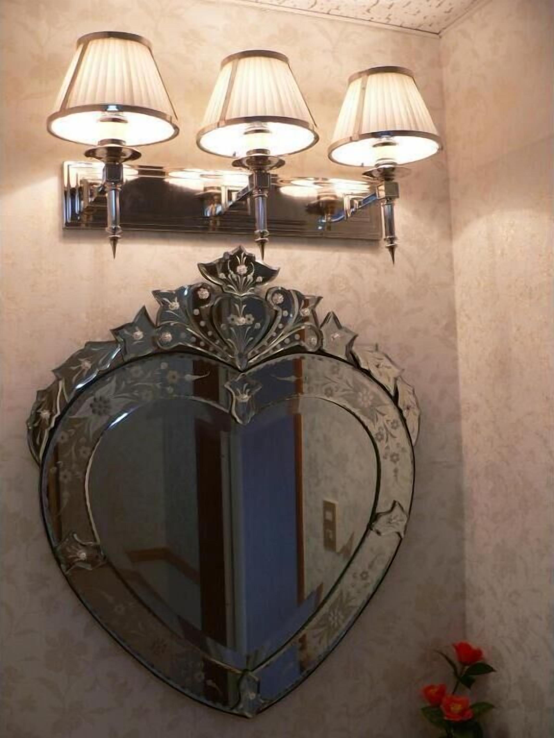 A heart-shaped mirror with a decorative frame and three wall-mounted lamps above it.
