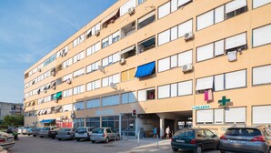 A multi-story building with a ground-level entrance, several parked cars, and a visible sign for a medical facility. - Comfortable and fully furbished apartment in center (Split)