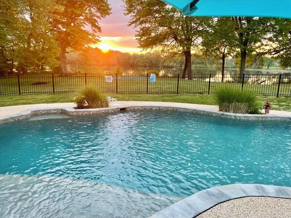 A swimming pool with a curved edge, surrounded by a fence and trees.