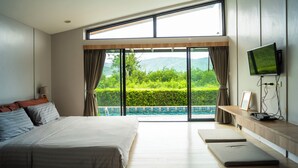 Quarto moderno com uma cama grande, televisão e vista para uma piscina e vegetação.