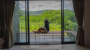Una habitación con un amplio ventanal corredero que da a un balcón con vistas a un paisaje verde exuberante.