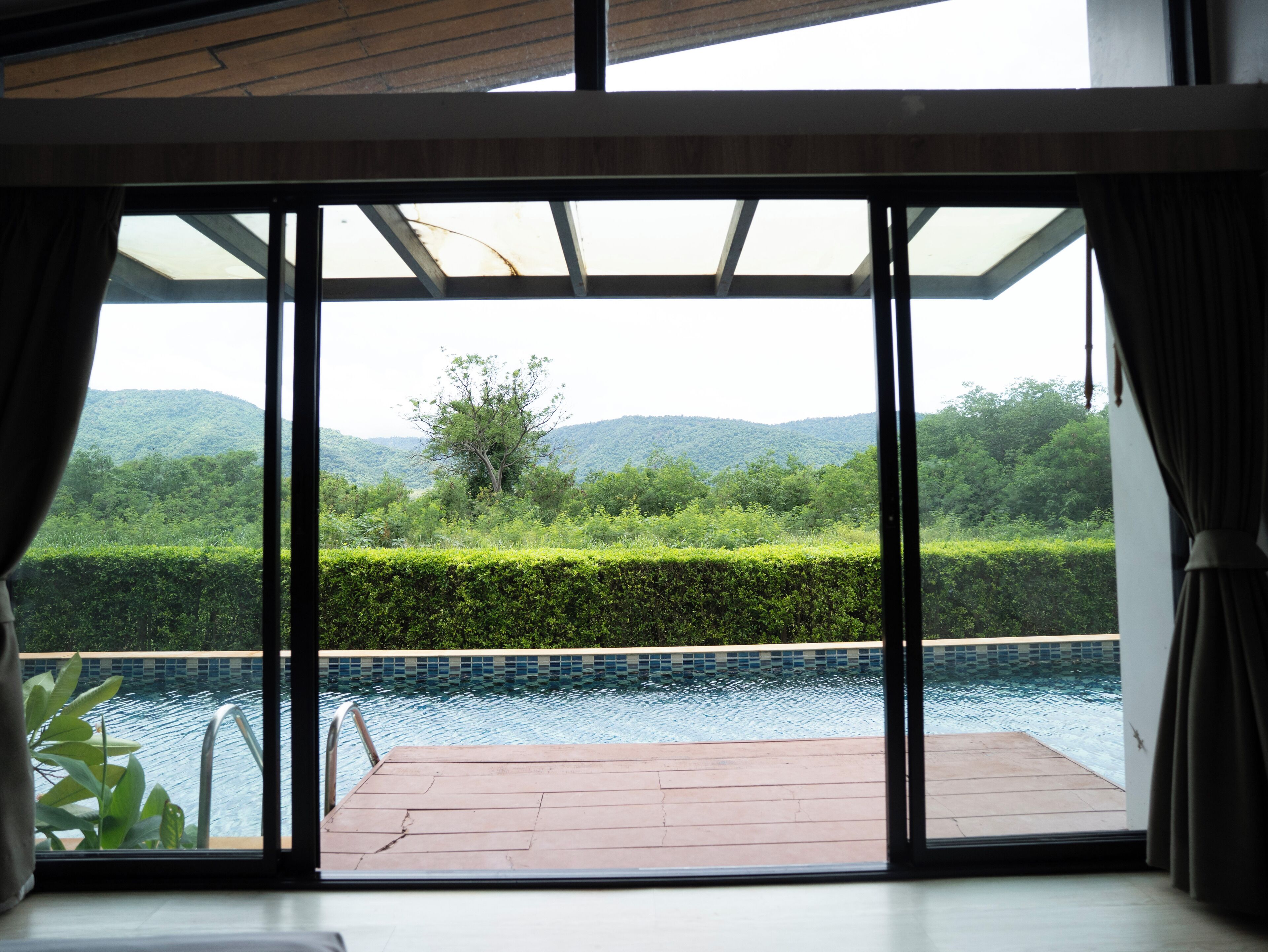 Habitación con un amplio ventanal corredero que da a una zona de piscina, vistas de exuberante vegetación y colinas, y una piscina con baldosas.