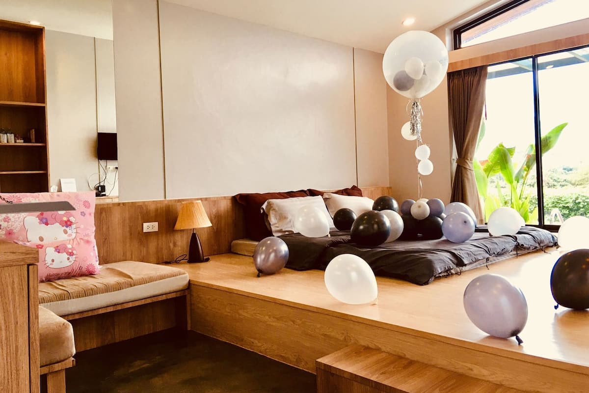 A modern bedroom with a bed, pillows, a bedside table, a lamp, and balloons.
