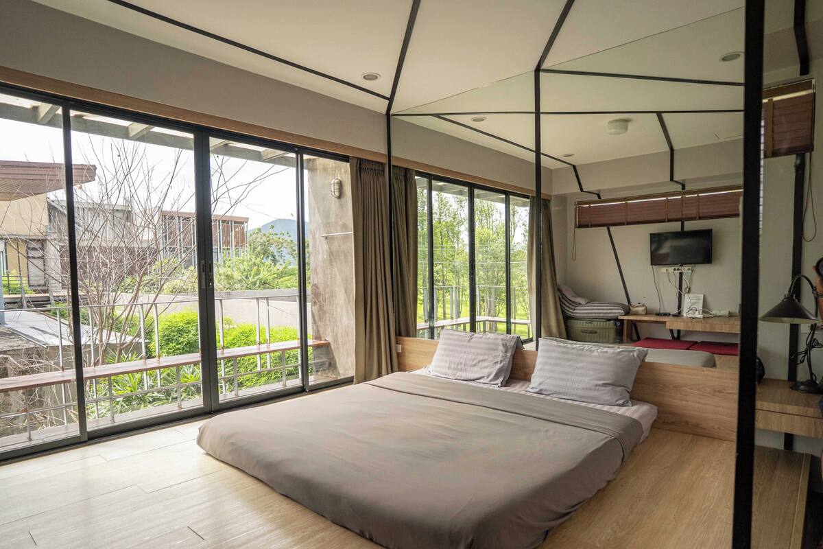A modern bedroom with a large bed, a desk with a computer, and a TV.