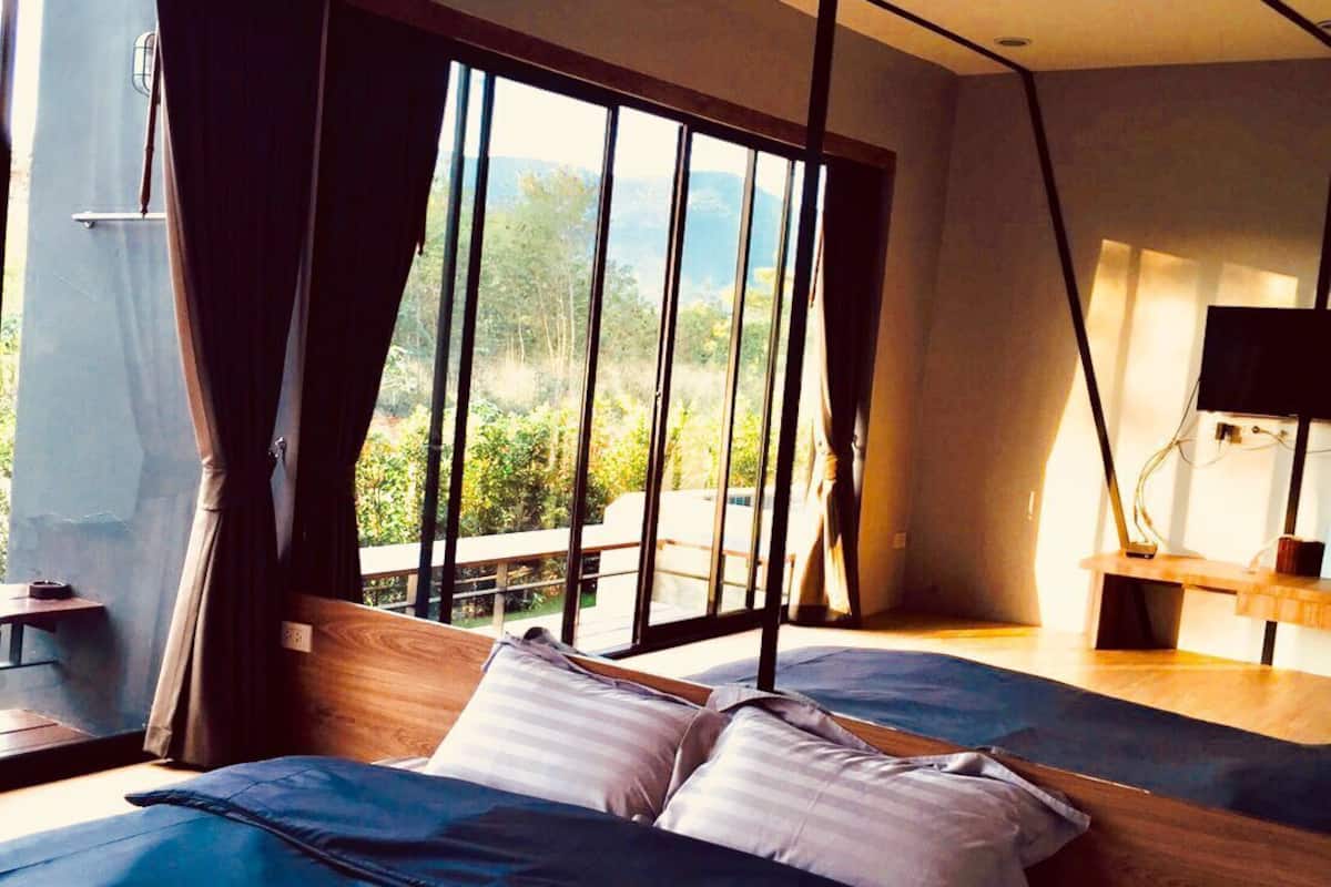 A modern bedroom with a large bed, a desk, and a view of greenery.