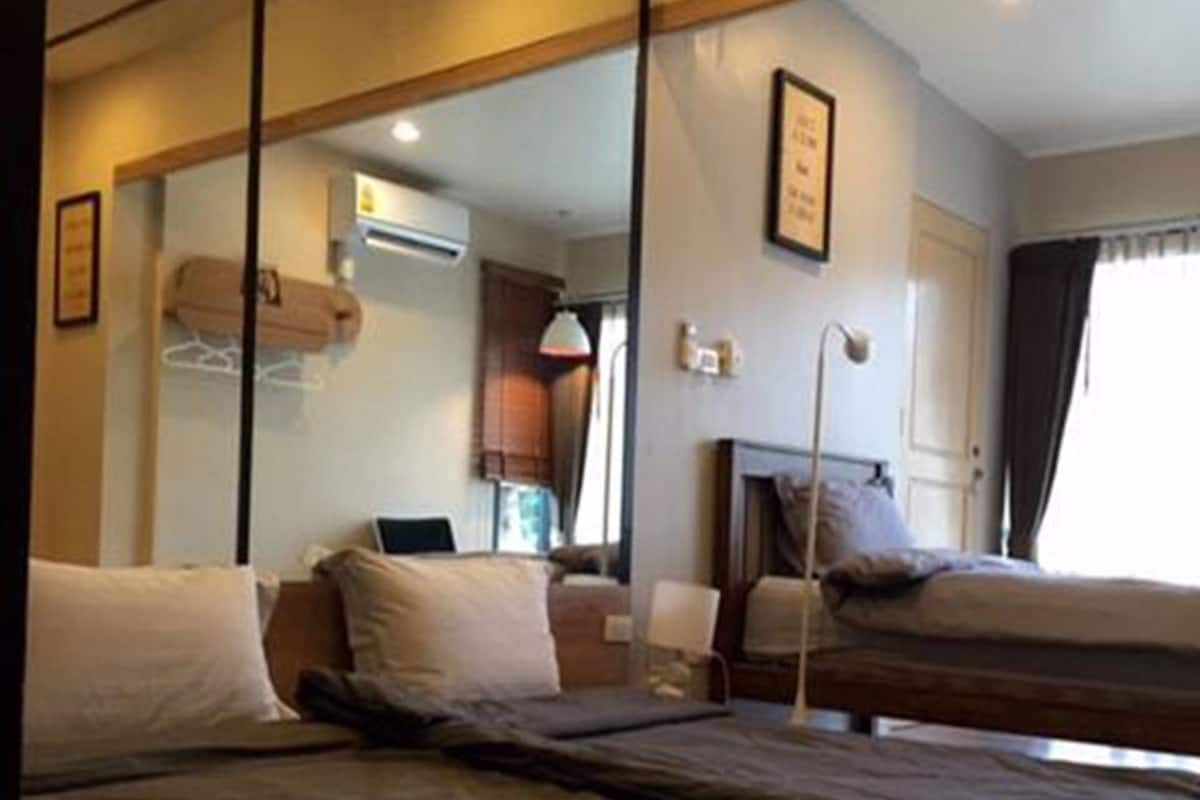 A room with a bed, a desk, and a chair. There is a mirror on the wall and a window with curtains.
