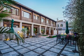 Un patio con suelo de baldosas, mobiliario exterior y un edificio con varias ventanas y balcones.