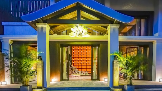 Entrada de hotel con diseño moderno, que presenta un amplio toldo, un accesorio de iluminación decorativo sobre la puerta y un camino empedrado que conduce a la entrada.