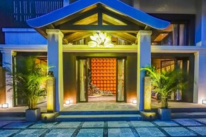 A hotel entrance with a modern design, featuring a large entrance canopy, a decorative light fixture above the door, and a tiled pathway leading to the entrance.