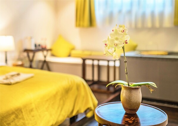 A hotel room with a bed, a small table with a vase of flowers, and a window with curtains.