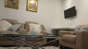 A living room with a sofa, a glass coffee table, and a television mounted on the wall. - Ambassador's Inn Next Door (Stratford)