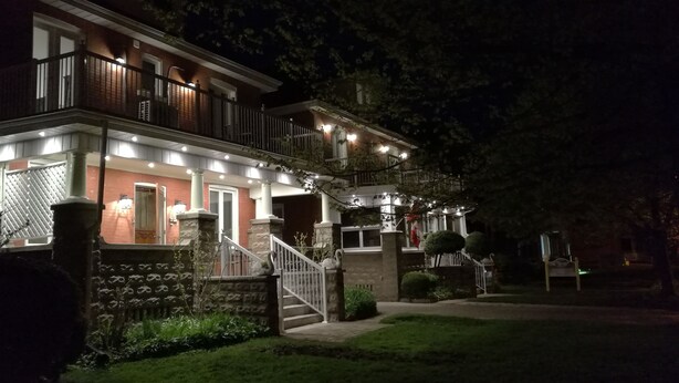 A two-story house with a balcony, a stone pillar, and a well-lit entrance. - Ambassador's Inn Next Door (Stratford)