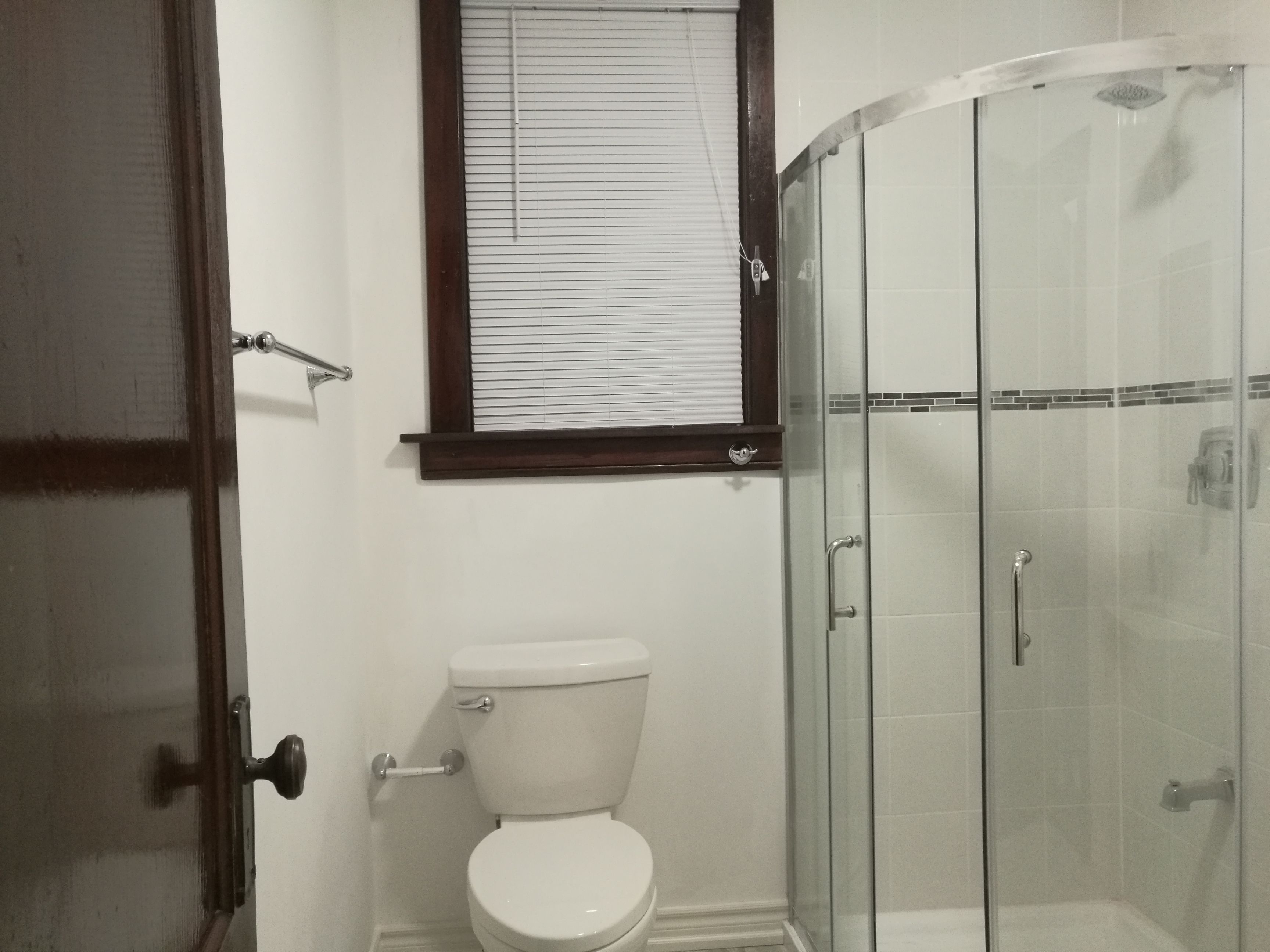 A bathroom with a toilet, a glass shower enclosure, and a window with blinds.