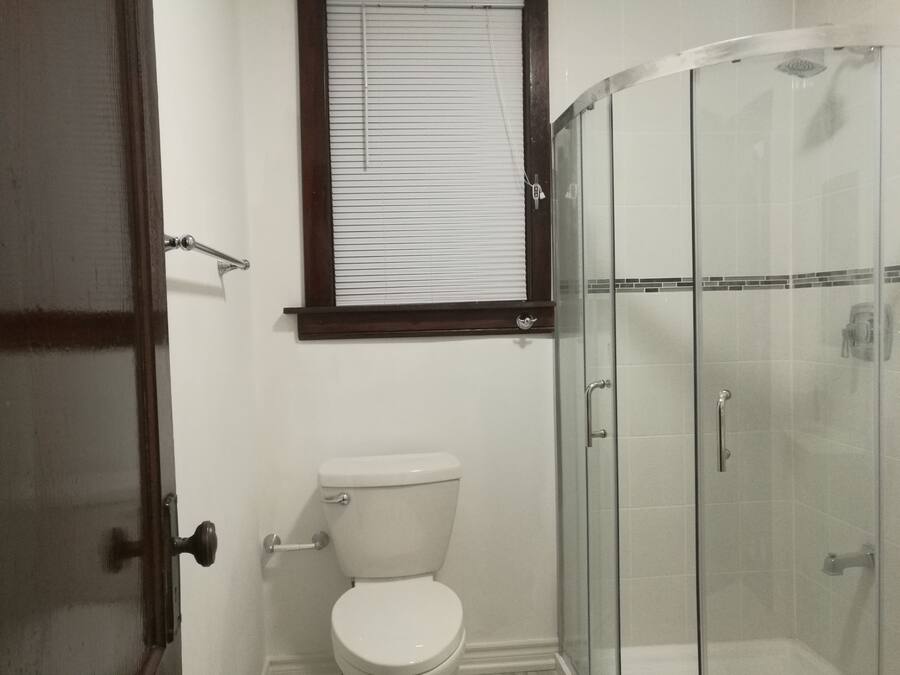 A bathroom with a toilet, a glass shower enclosure, and a window with blinds.