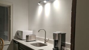 A kitchen with a white countertop, a stainless steel sink, a microwave, a toaster, and a coffee maker. - Ambassador's Inn Next Door (Stratford)