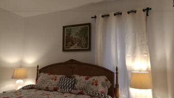 A bedroom with a wooden bed, floral bedding, a painting on the wall, and two bedside lamps.