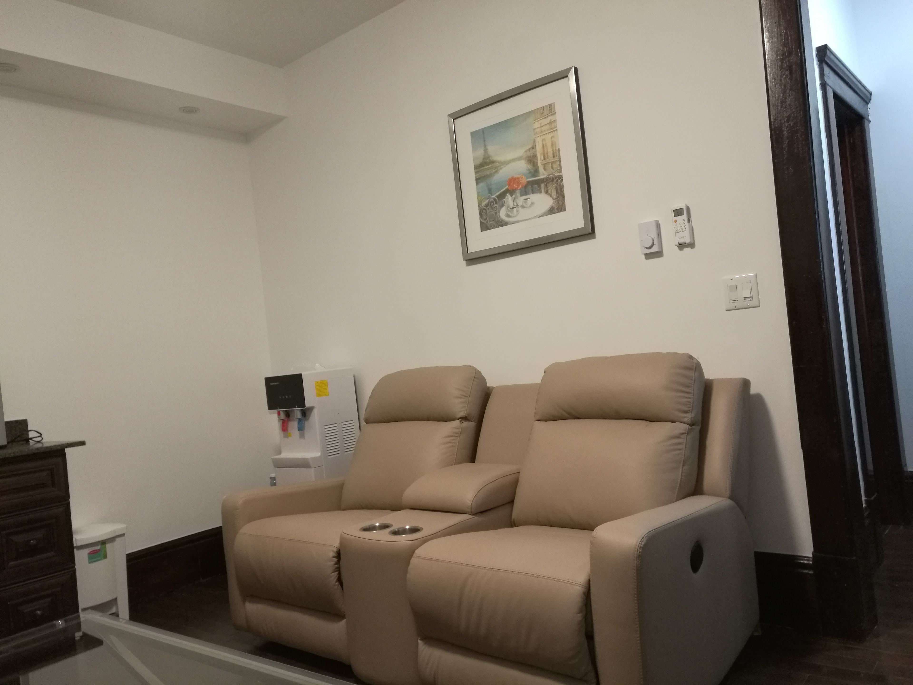 Habitación con sillón de masajes, dispensador de agua y un cuadro en la pared.