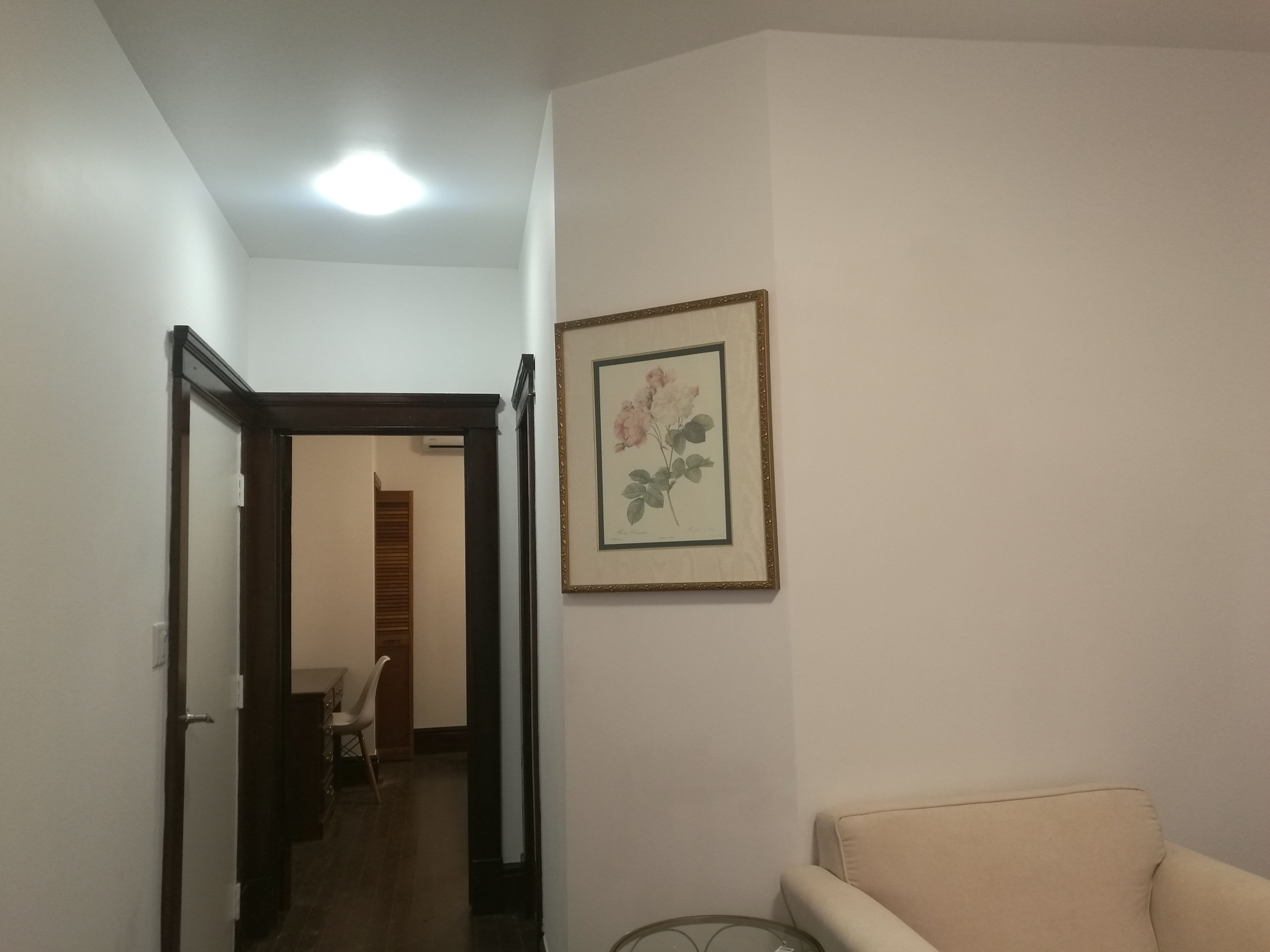 A hallway with a door leading to a dining area, a framed picture on the wall, and a beige armchair.
