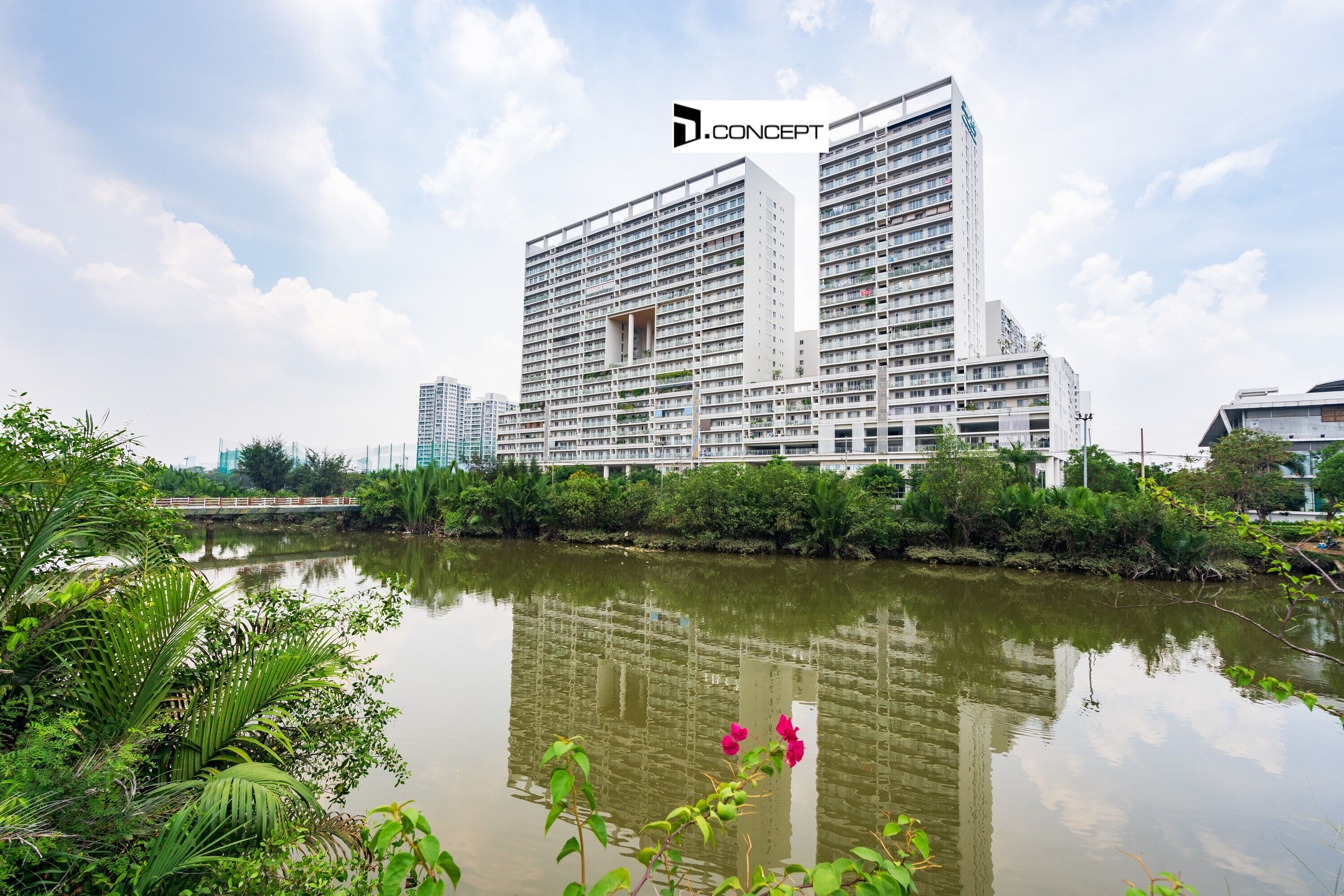 Ein modernes Hochhaus-Hotel mit mehreren Balkonen, gelegen am Ufer eines ruhigen Flusses mit üppiger Vegetation und blauem Himmel.
