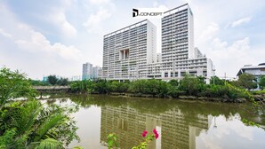 Un moderno hotel de gran altura con varios balcones, ubicado junto a un río tranquilo, exuberante vegetación y un cielo despejado.