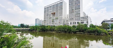 Un moderno hotel de gran altura con varios balcones, ubicado junto a un río tranquilo, exuberante vegetación y un cielo despejado.