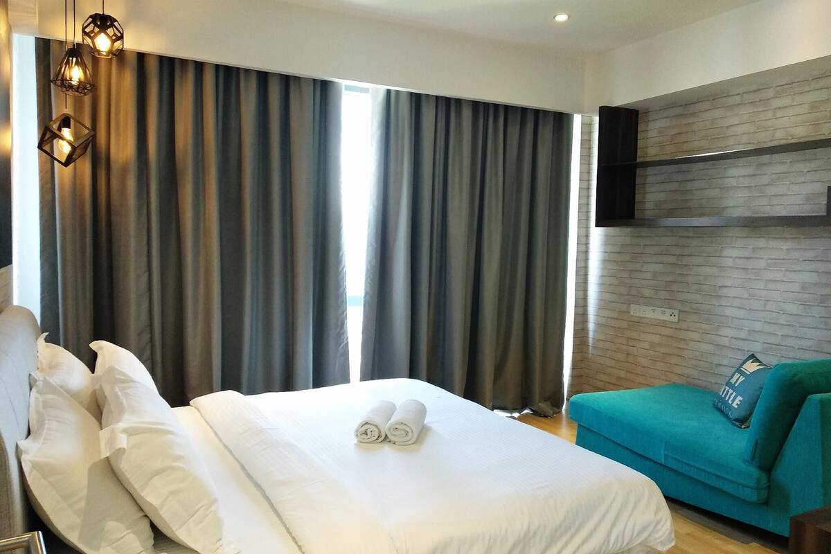 A hotel room with a bed, curtains, a teal sofa, and a mounted TV.