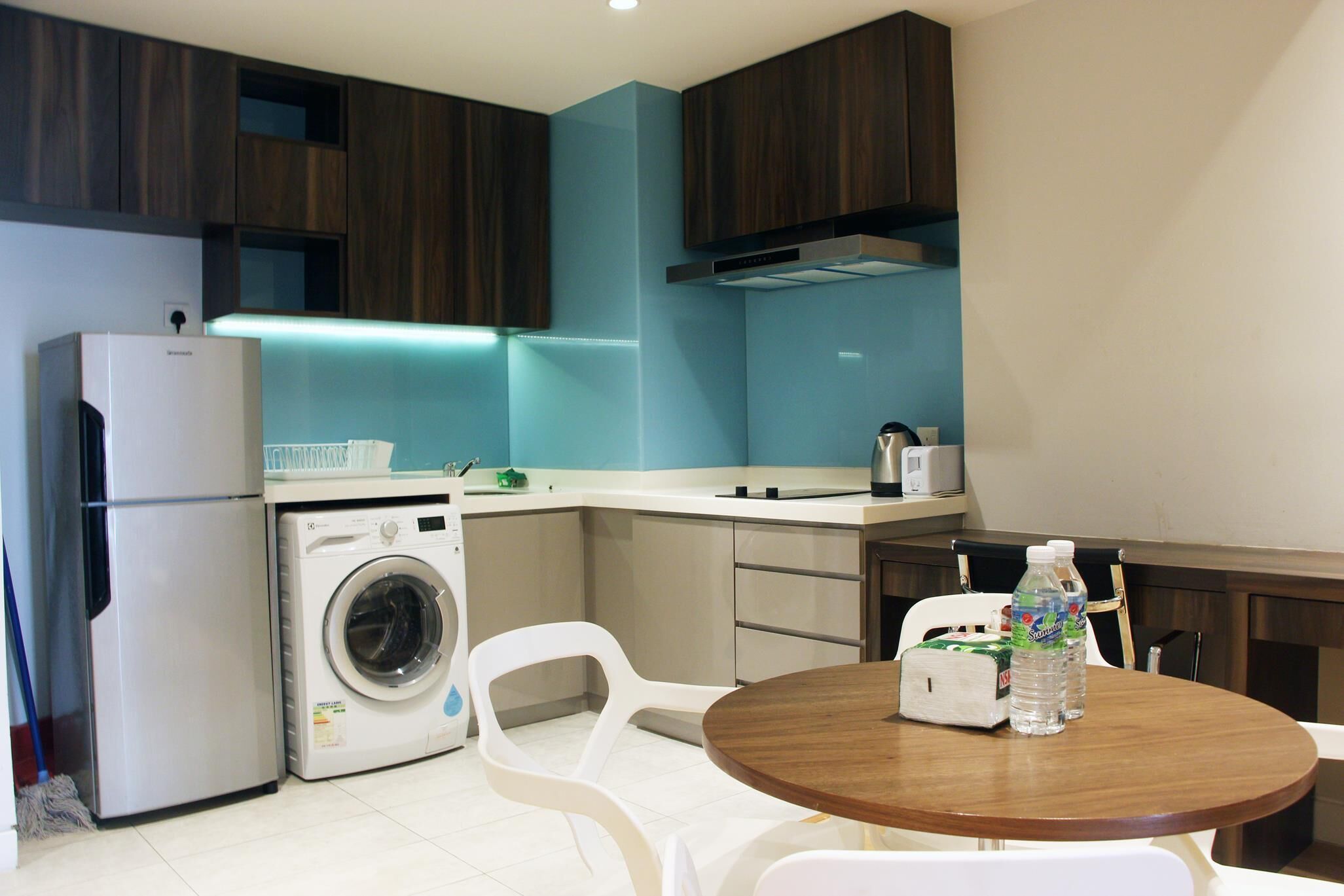 A compact kitchen with a washing machine, a refrigerator, and a dining area with a table and chairs.