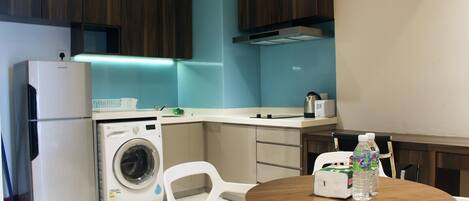 A compact kitchen with a washing machine, a refrigerator, and a dining area with a table and chairs.