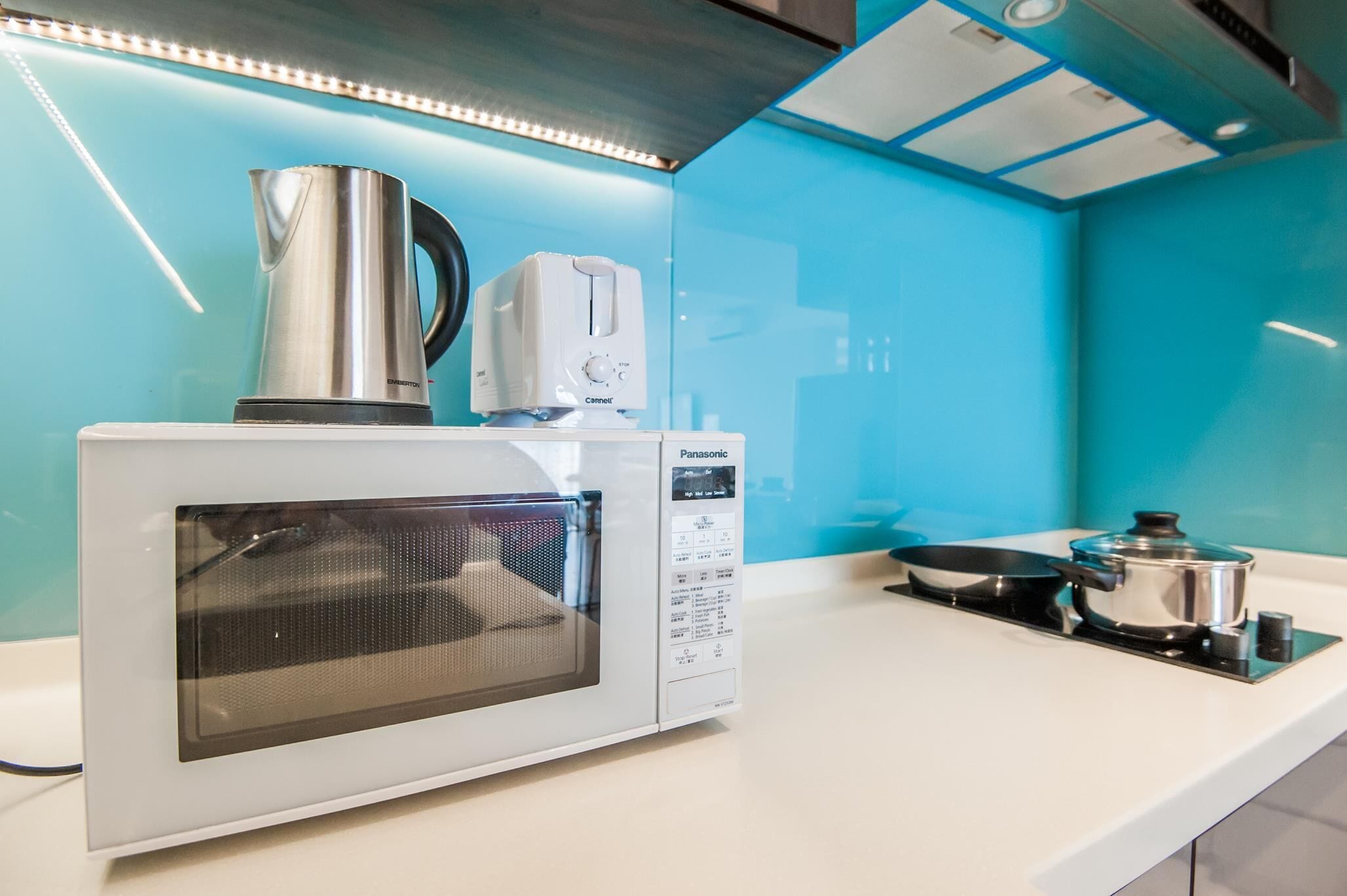 Une cuisine moderne avec un micro-ondes blanc, un grille-pain et une bouilloire posés sur le plan de travail, ainsi qu'une cuisinière avec des casseroles et des poêles.