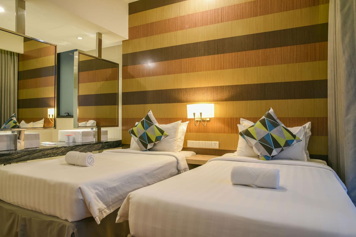 A hotel room with two beds, a large mirror, and a wooden striped wall.