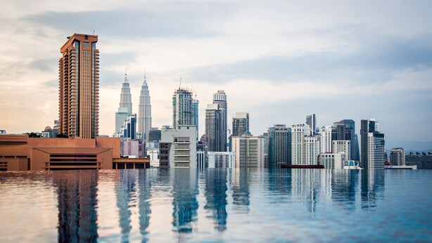 A city skyline reflected in a body of water with high-rise buildings, including a prominent tower. - D'Majestic Place by Widebed (Kuala Lumpur)