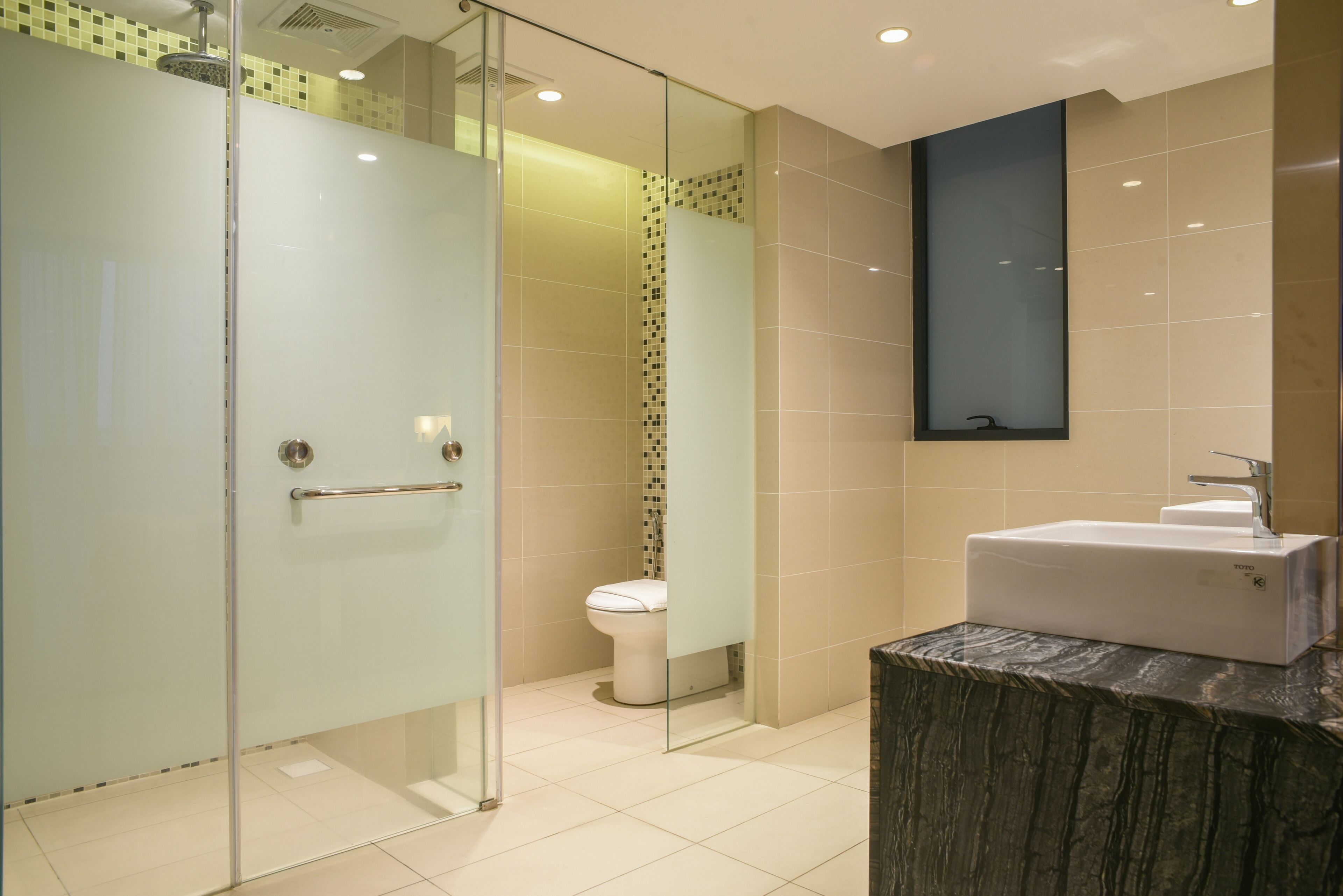 Une salle de bain moderne dotée d’une douche à parois de verre, de toilettes et d’un lavabo avec un plan de travail en marbre.