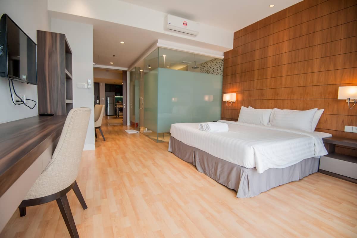 A modern hotel room with a large bed, a desk with a chair, a TV mounted on the wall, and a wooden accent wall.